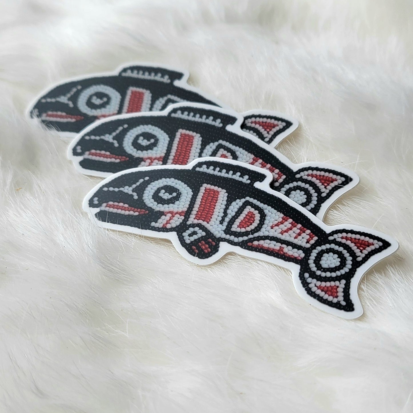 A sticker of a beaded formline style fish it has black outlines that are filled in with white and red formline shapes.