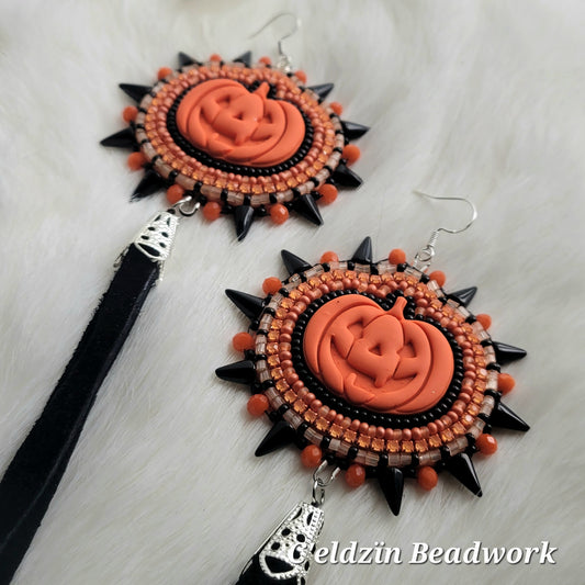 Orange clay jack o lantern glued onto beading foundation. One row of black beads embroidered all around it, one row of light orange and medium matte orange beads, a row of orange rhinestone banding, and the last row being crystal orange and opaque black beads. It is edged with orange rondelle beads and black spike beads. It has a silver earring hook on top and a silver cone with black deer hide fringe on the bottom.